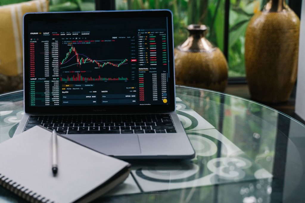 cryptocurrency-chart-displayed-on-a-laptop-14751274 Laptop displaying cryptocurrency stocks and graphs on a glass table with a notepad.